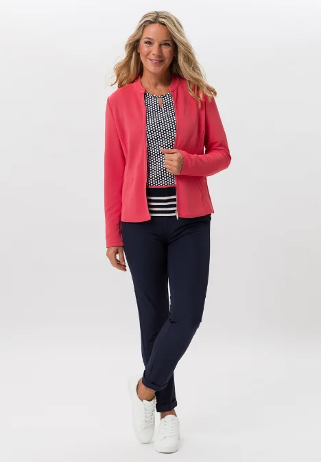 Dame mit einer roten Jacke, bemustertes T-Shirt und dunklen Hose