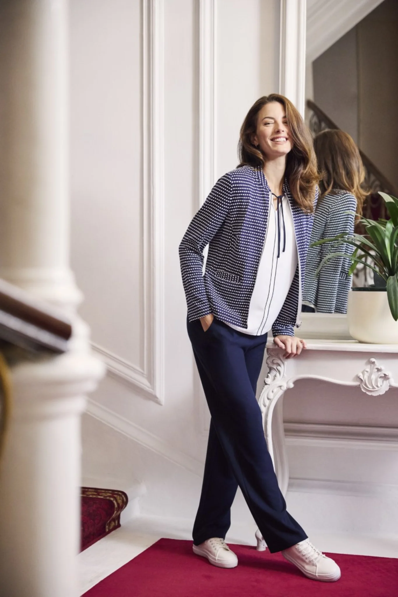 Dame die eine bepunktete Jacke, eine weiße Bluse und eine dunkelblaue Hose trägt