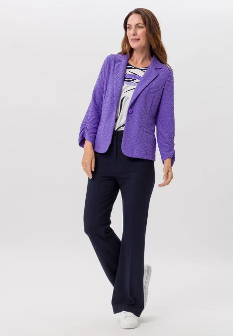 Dame mit lila Jacke, bemusterten Shirt und schwarzer Hose